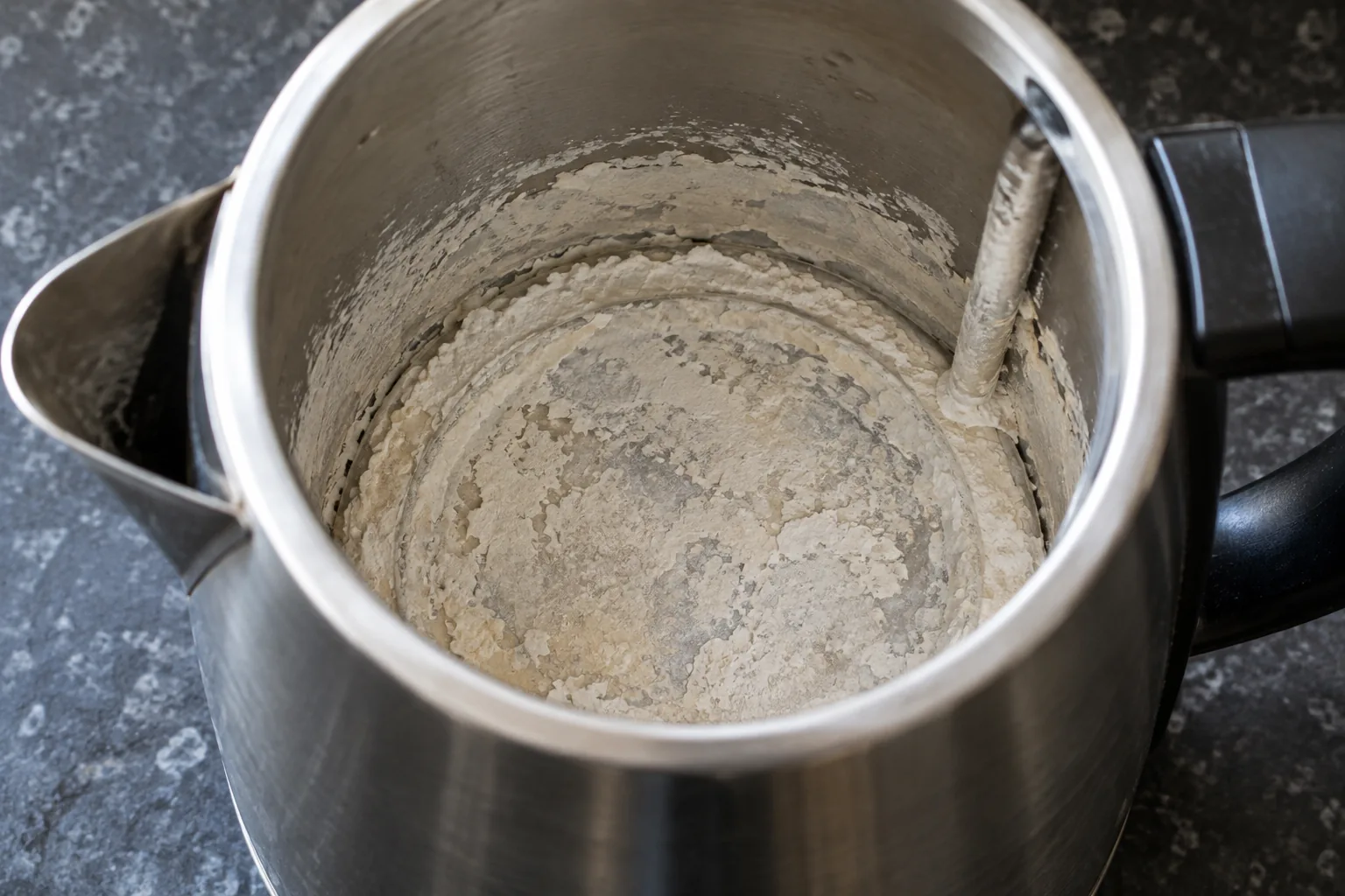 Close-up inside an open kettle showing the element and base furred with thick white limescale